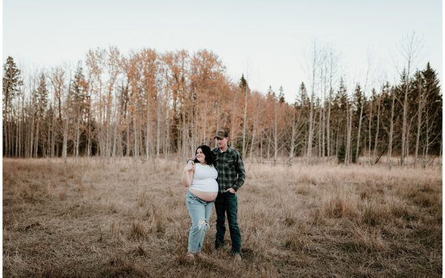 Maternity couple standing in a field in late fall.