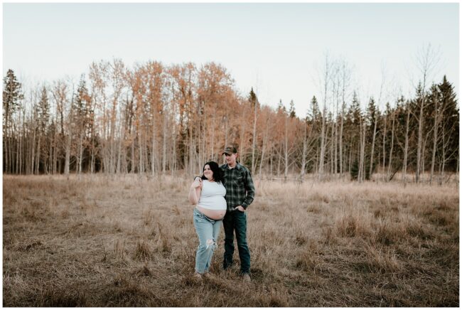 Maternity couple standing in a field in late fall.